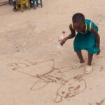 child using a water bottle to make pictures in the sand